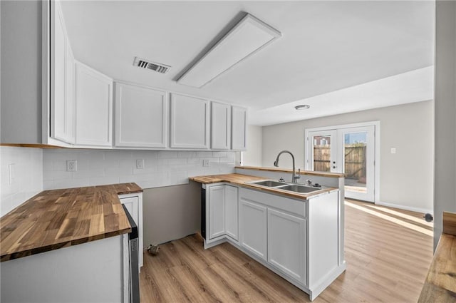 kitchen featuring sink, butcher block counters, kitchen peninsula, and white cabinetry