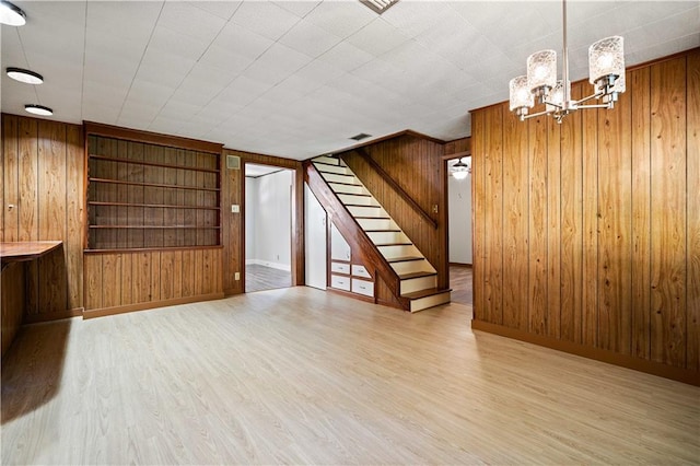 unfurnished living room featuring a chandelier, light hardwood / wood-style flooring, built in shelves, and wood walls