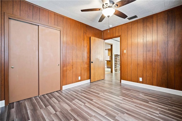 unfurnished bedroom with a closet, ceiling fan, light wood-type flooring, and wooden walls