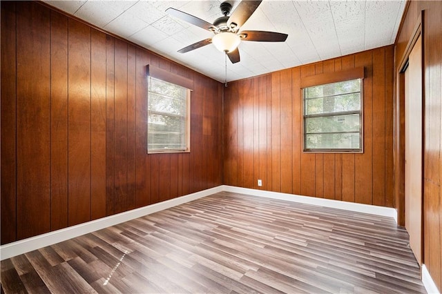 unfurnished room featuring hardwood / wood-style floors, wooden walls, and ceiling fan