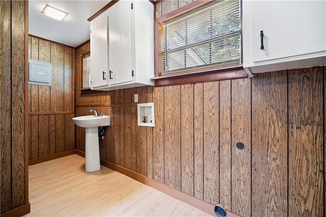 clothes washing area featuring washer hookup, light hardwood / wood-style flooring, sink, cabinets, and wood walls