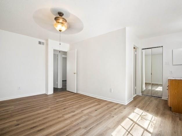 unfurnished bedroom featuring a ceiling fan, visible vents, baseboards, and wood finished floors