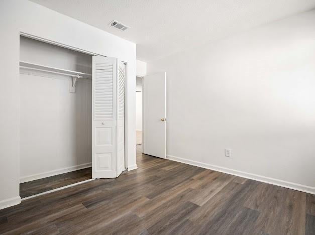 unfurnished bedroom with a closet, visible vents, baseboards, and wood finished floors