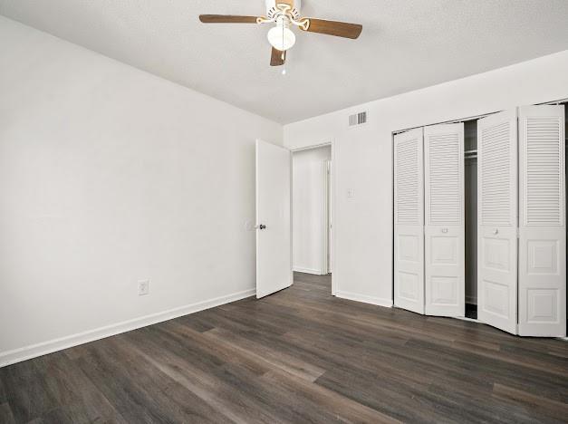 unfurnished bedroom with dark wood-style floors, baseboards, visible vents, and ceiling fan