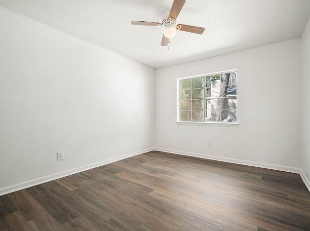 empty room with dark wood-type flooring, a ceiling fan, and baseboards