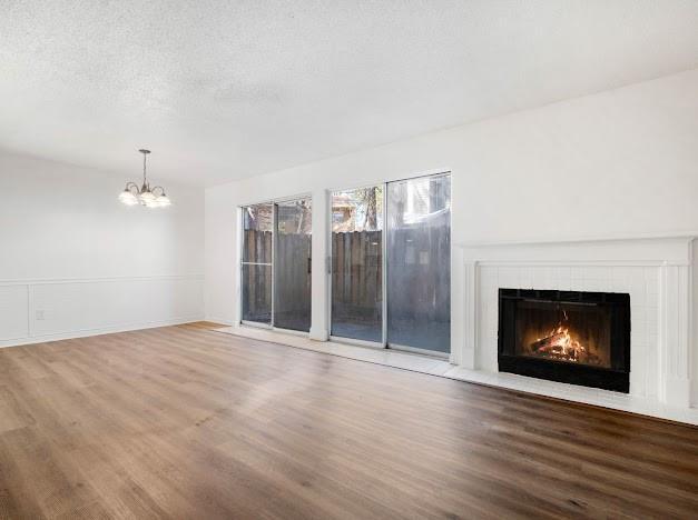 unfurnished living room featuring a textured ceiling, wood finished floors, a tile fireplace, and an inviting chandelier