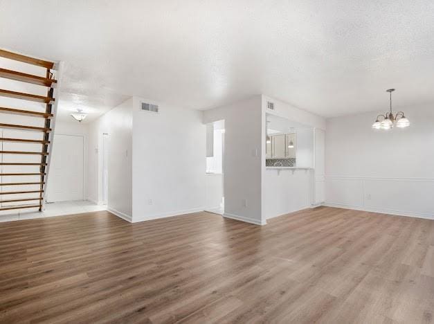 unfurnished living room featuring a notable chandelier, stairs, visible vents, and wood finished floors