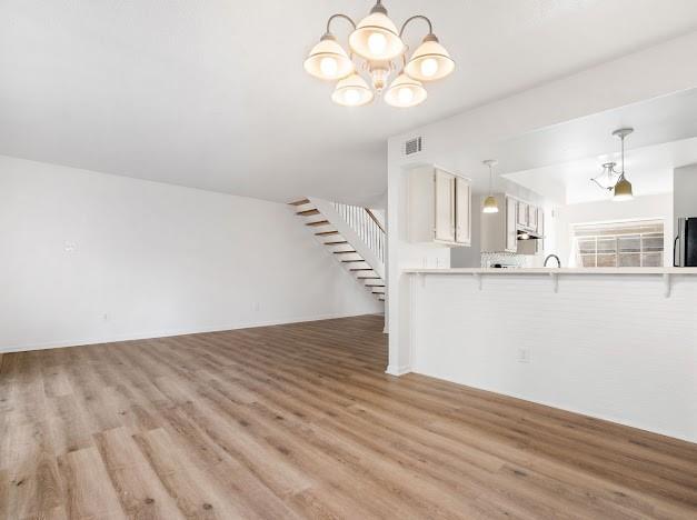 unfurnished living room with light wood-type flooring, stairs, visible vents, and a notable chandelier