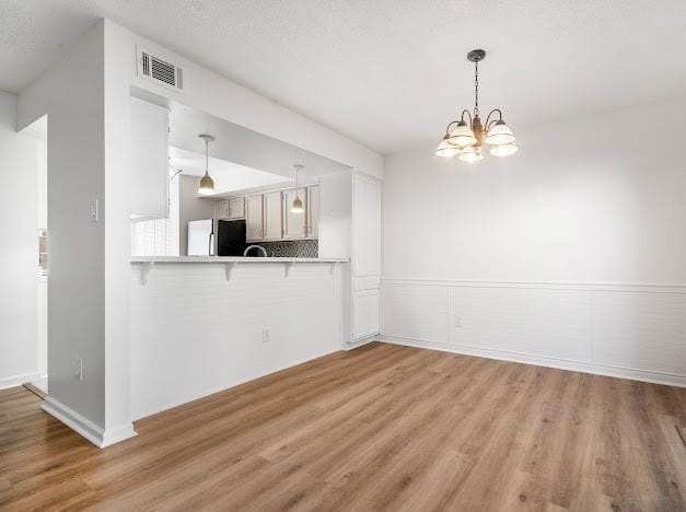 kitchen with a breakfast bar area, light countertops, visible vents, light wood-type flooring, and fridge