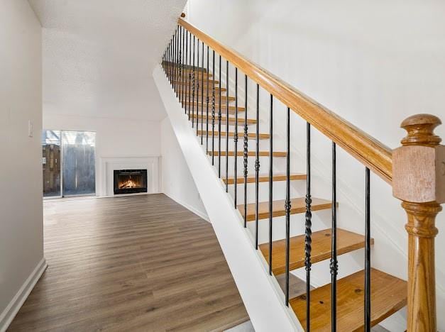 staircase featuring a lit fireplace, baseboards, and wood finished floors