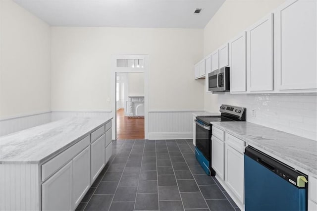 1012 Texas St, Mobile, AL 36604 - kitchen featuring dark tile patterned flooring, a wainscoted wall, light stone counters, white cabinets, and appliances with stainless steel finishes
