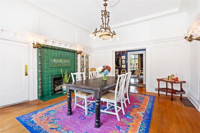 dining room with a tiled fireplace, an inviting chandelier, ornamental molding, and wood-type flooring