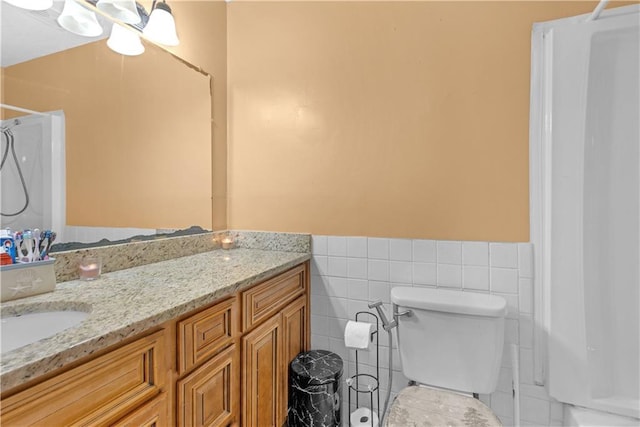 bathroom with vanity, a shower, toilet, and tile walls