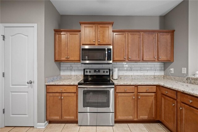 kitchen with backsplash, light stone countertops, light tile patterned flooring, and appliances with stainless steel finishes