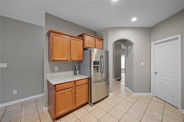 kitchen with stainless steel fridge with ice dispenser, light tile patterned floors, and light stone countertops