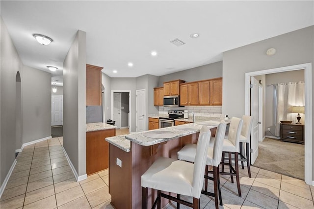 kitchen with kitchen peninsula, a breakfast bar, stainless steel appliances, and light stone counters