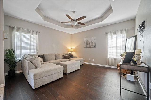 living room with a raised ceiling, ceiling fan, and dark hardwood / wood-style flooring