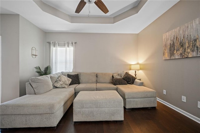 living room featuring dark hardwood / wood-style flooring, a raised ceiling, and ceiling fan