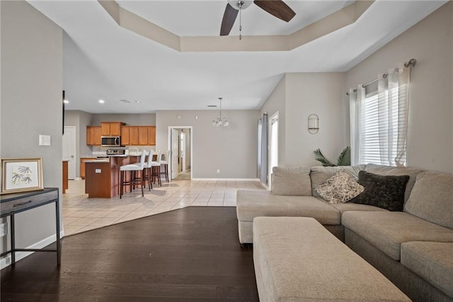 living room with a raised ceiling, light hardwood / wood-style floors, and ceiling fan with notable chandelier