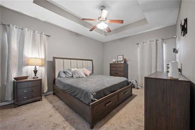 carpeted bedroom with a raised ceiling and ceiling fan