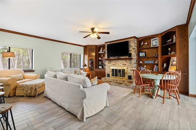 living area with ceiling fan, light wood-style flooring, a fireplace, built in features, and ornamental molding