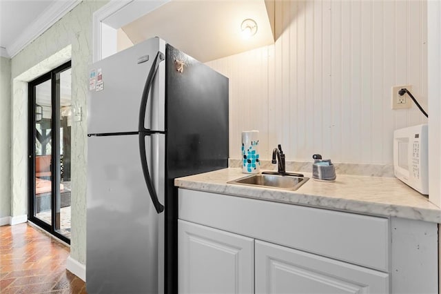 kitchen featuring white microwave, freestanding refrigerator, brick floor, crown molding, and a sink