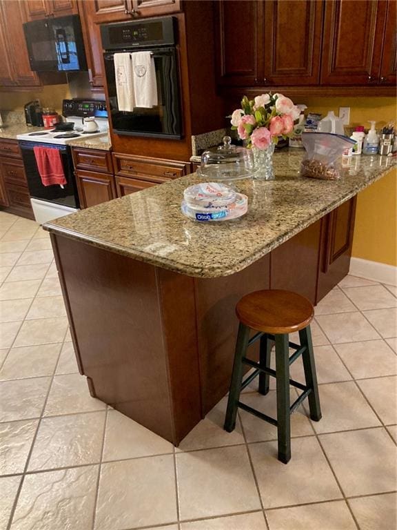 kitchen with light tile patterned flooring, a breakfast bar area, black appliances, and light stone counters