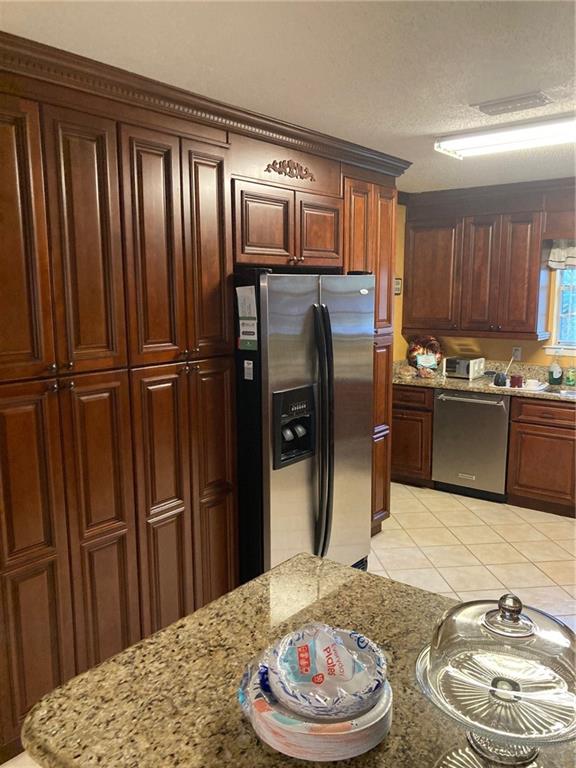 kitchen featuring a textured ceiling, appliances with stainless steel finishes, light tile patterned flooring, and light stone countertops