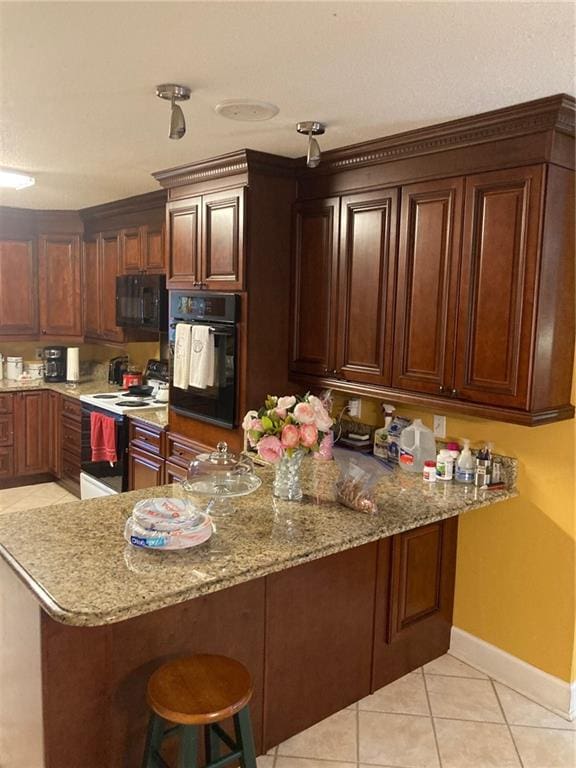 kitchen featuring black appliances, kitchen peninsula, a kitchen breakfast bar, light stone countertops, and light tile patterned floors