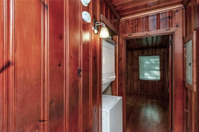 washroom featuring electric panel, stacked washing maching and dryer, and wood walls