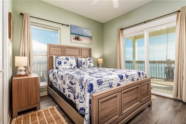 bedroom with dark wood-style floors, access to outside, multiple windows, and a water view