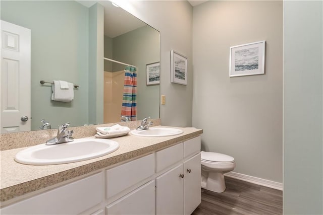 bathroom featuring double vanity, wood finished floors, a sink, and toilet