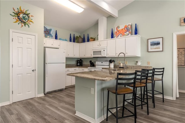 kitchen with white appliances, white cabinetry, a sink, and a peninsula