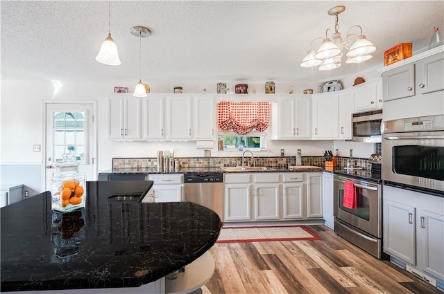 kitchen with sink, light wood-type flooring, decorative light fixtures, and appliances with stainless steel finishes