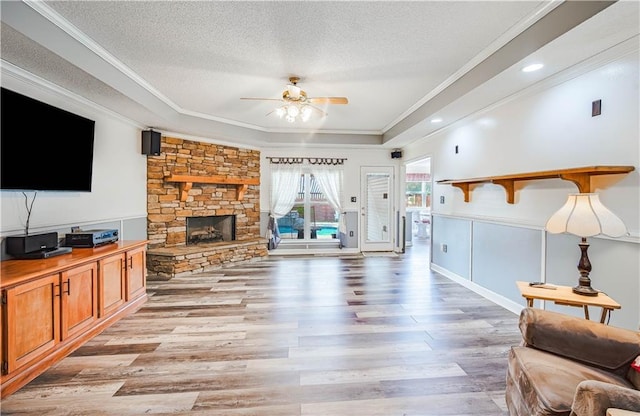 living room featuring light hardwood / wood-style flooring, ceiling fan, ornamental molding, and a stone fireplace