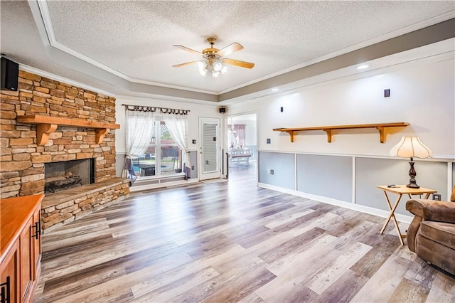 living room featuring a textured ceiling, light hardwood / wood-style floors, a stone fireplace, and ornamental molding