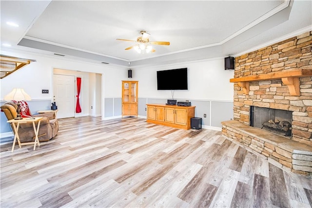 living room featuring a stone fireplace, crown molding, light hardwood / wood-style flooring, and ceiling fan