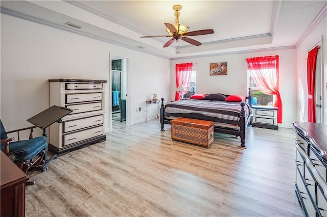 bedroom with ensuite bath, light hardwood / wood-style flooring, ceiling fan, ornamental molding, and a tray ceiling