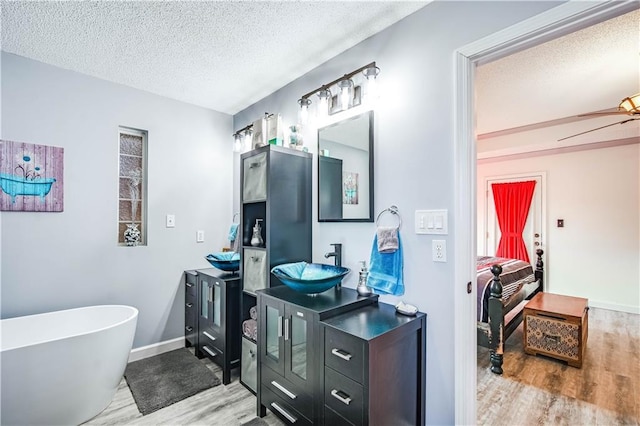 bathroom with vanity, ceiling fan, a tub to relax in, a textured ceiling, and wood-type flooring