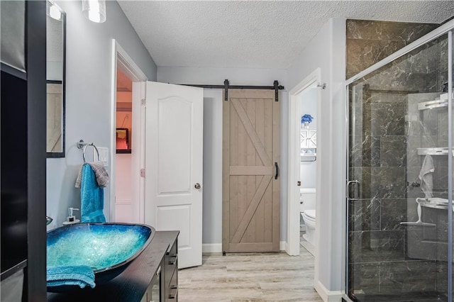 bathroom featuring hardwood / wood-style floors, a textured ceiling, toilet, a shower with door, and vanity