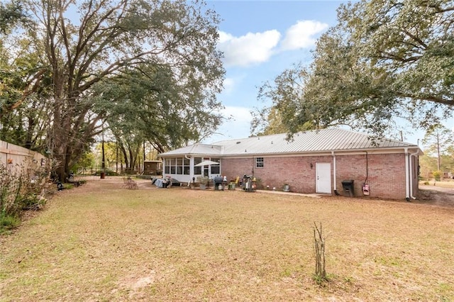 back of property with brick siding, a yard, a sunroom, metal roof, and fence