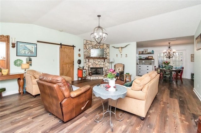 living area with a notable chandelier, lofted ceiling, a barn door, a stone fireplace, and wood finished floors