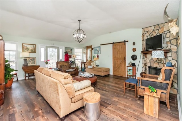 living room featuring lofted ceiling, wood finished floors, a stone fireplace, and a barn door