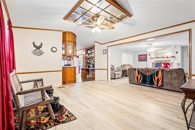 living room featuring hardwood / wood-style flooring, ceiling fan, crown molding, and a textured ceiling