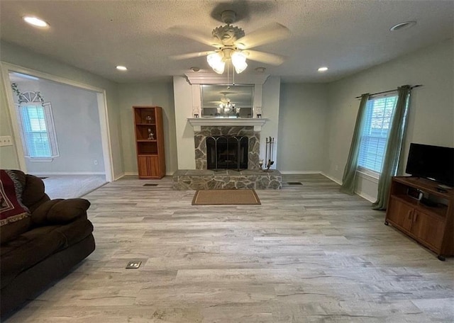 living room with a stone fireplace, ceiling fan, light hardwood / wood-style flooring, and a textured ceiling