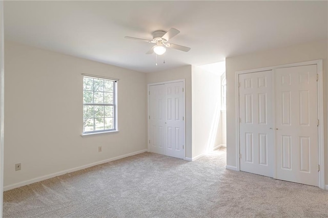 unfurnished bedroom featuring ceiling fan, light colored carpet, and multiple closets