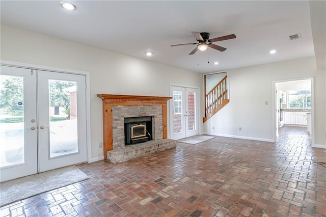 unfurnished living room with a brick fireplace, french doors, and ceiling fan