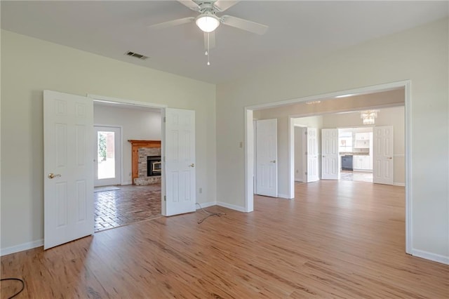 unfurnished living room featuring a brick fireplace, ceiling fan, and light hardwood / wood-style floors