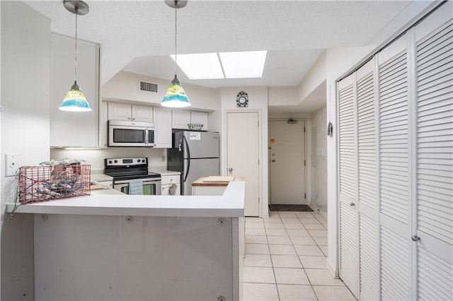 kitchen with appliances with stainless steel finishes, a skylight, light tile flooring, and pendant lighting