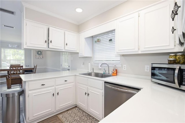 kitchen with sink, stainless steel appliances, ornamental molding, white cabinets, and kitchen peninsula